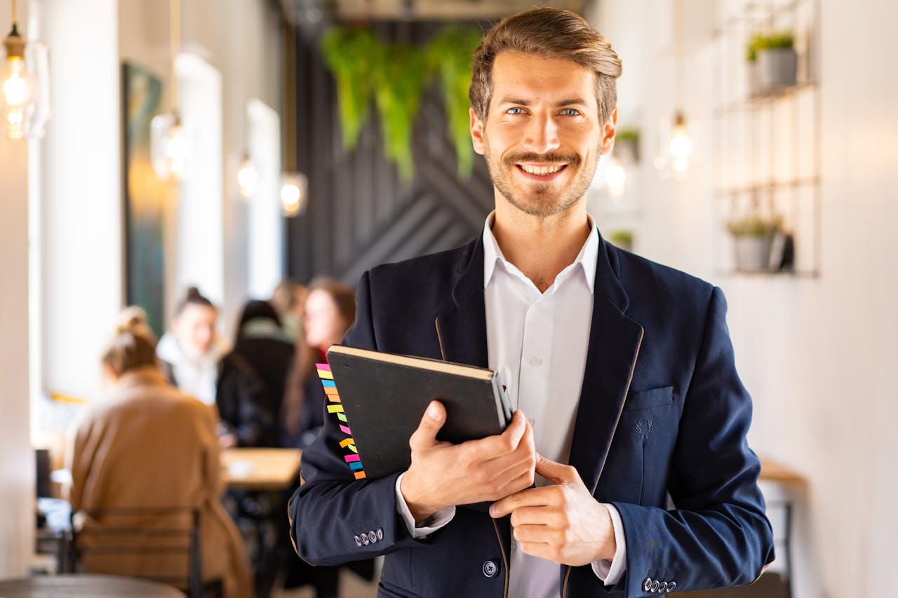 Homme souriant en costume bleu tenant un carnet, illustrant la comparaison entre assurance vie et contrat de capitalisation.