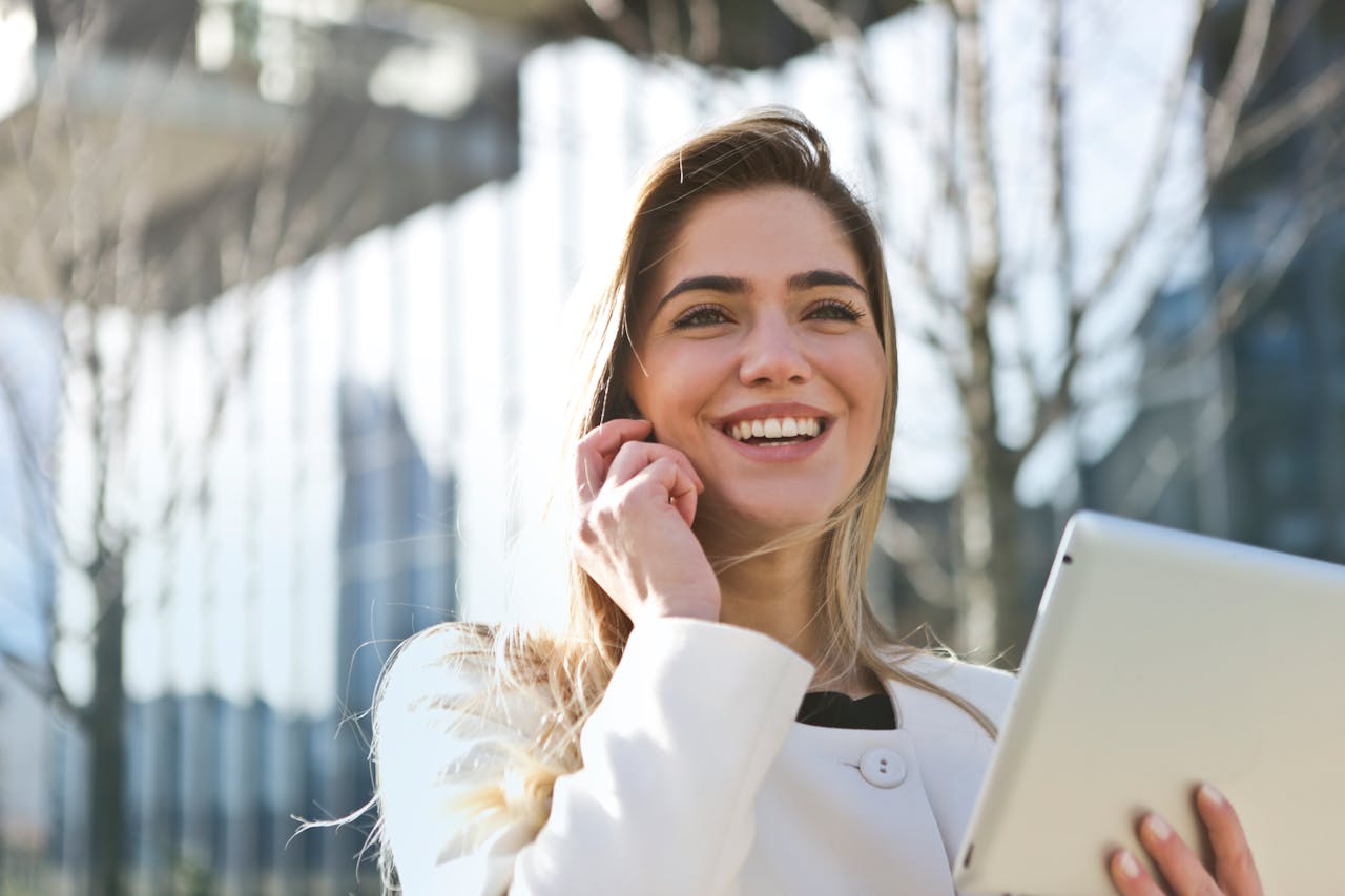 Femme en blazer blanc tenant une tablette, illustrant la gestion en ligne et le transfert d’un PEA vers un autre établissement.