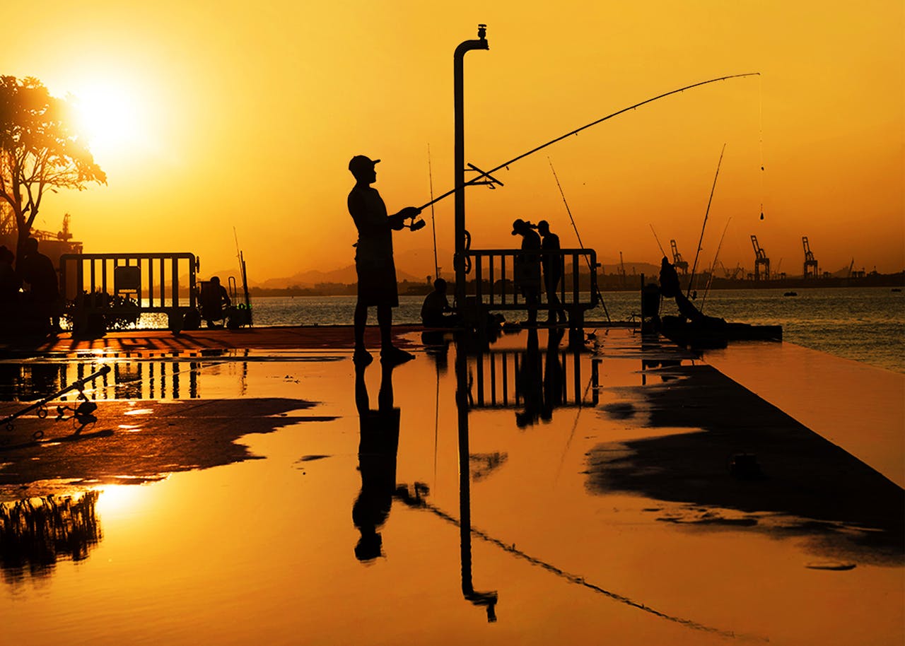 Silhouettes de pêcheurs au coucher du soleil à l’étranger, symbolisant la réflexion avant une expatriation et la gestion de son assurance vie.