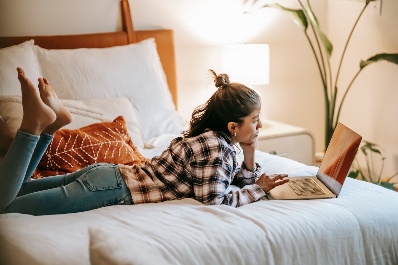 Femme utilisant un ordinateur portable depuis son lit, illustrant la gestion en ligne et l’investissement dans des ETF pour expatriés.
