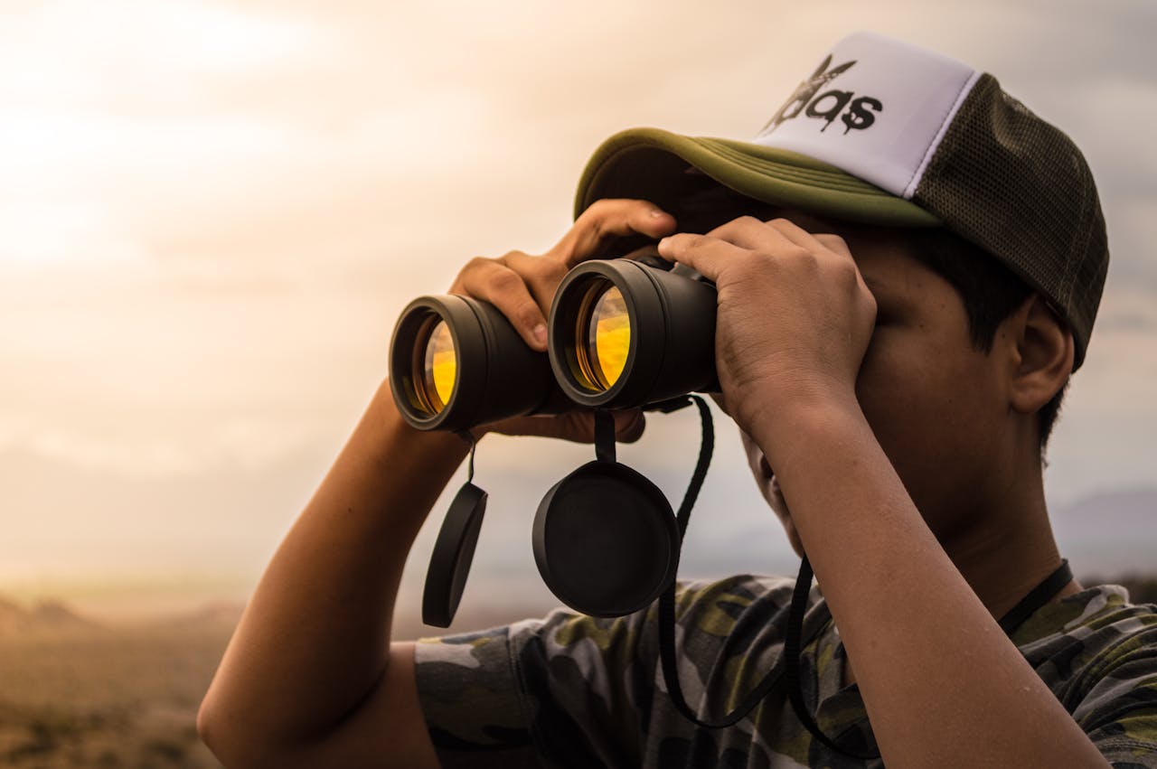 Homme regardant au loin avec des jumelles au coucher du soleil, symbolisant la vigilance face aux placements risqués pour les expatriés.