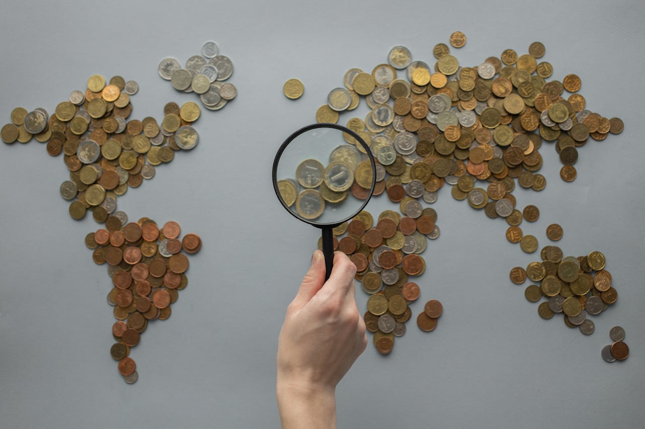 Loupe posée sur une carte du monde remplie de pièces, illustrant la fiscalité internationale d’un compte-titres ordinaire détenu à l’étranger.