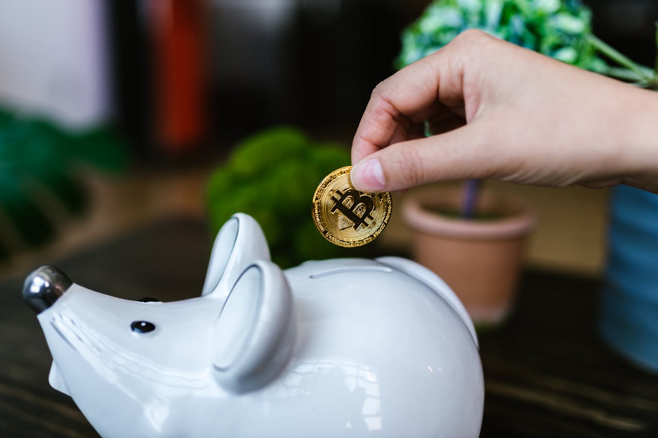 Main plaçant une pièce de Bitcoin dans une tirelire en forme de souris, illustrant la fiscalité des cryptomonnaies pour les expatriés.