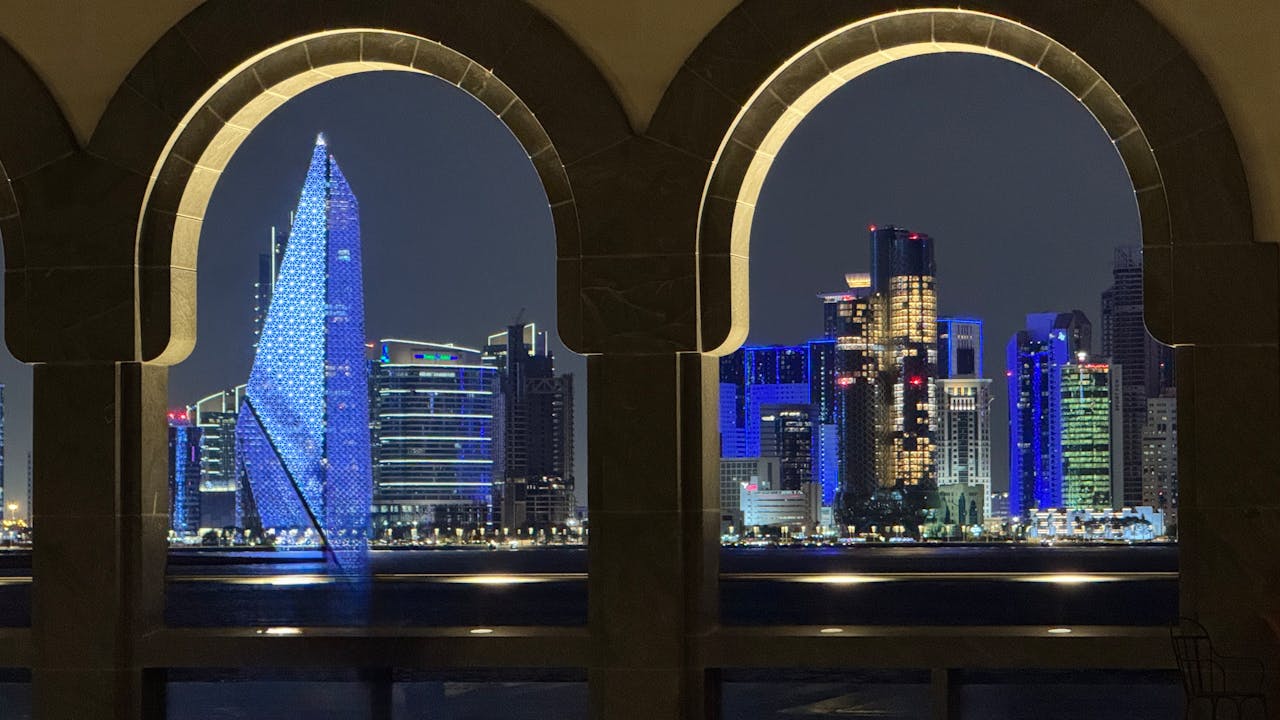Vue nocturne de la skyline de Doha à travers des arches architecturales, illustrant l’expatriation au Qatar et le choix d’une assurance vie internationale.